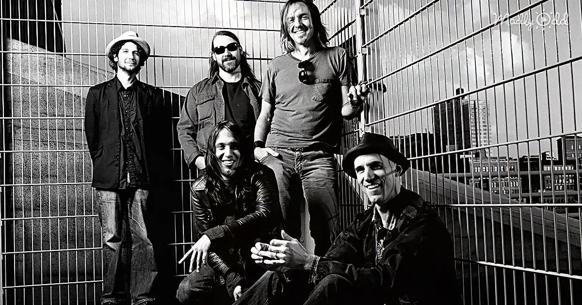 A black-and-white photo of five smiling individuals, three standing and two sitting, against a metal fence backdrop.