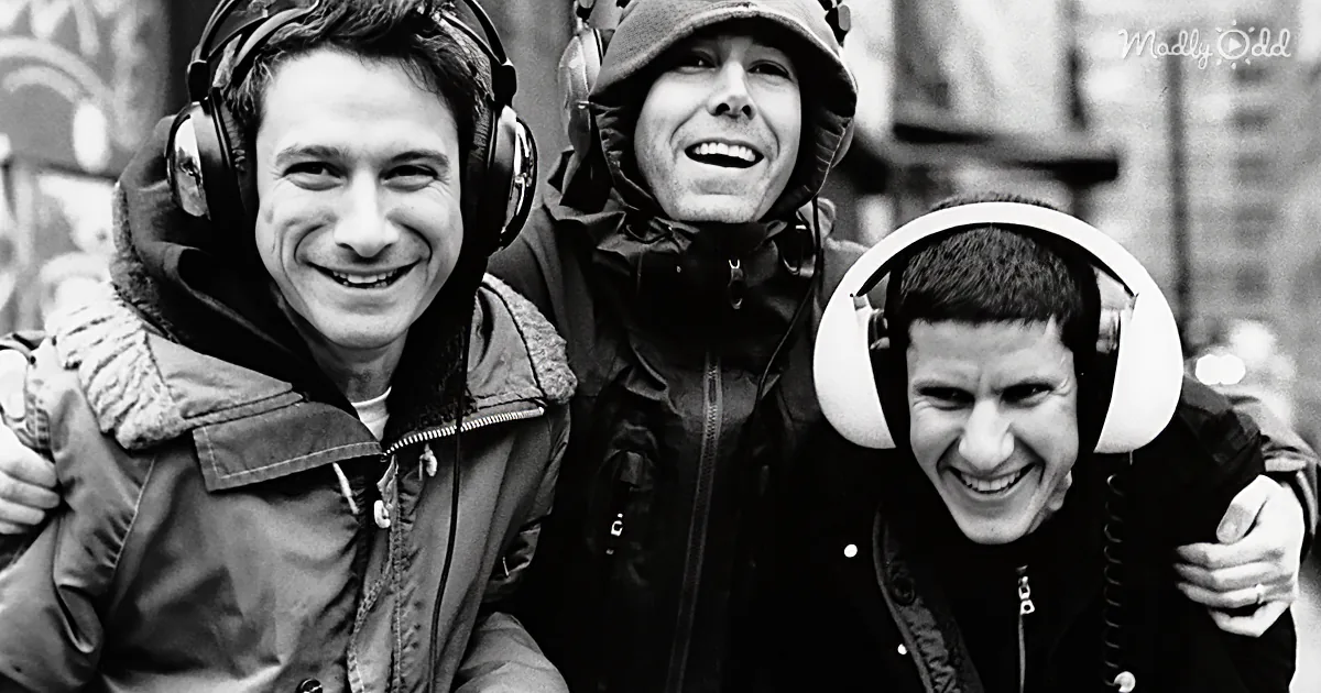 Three men in winter gear with headphones, smiling and embracing, in a black-and-white photo.