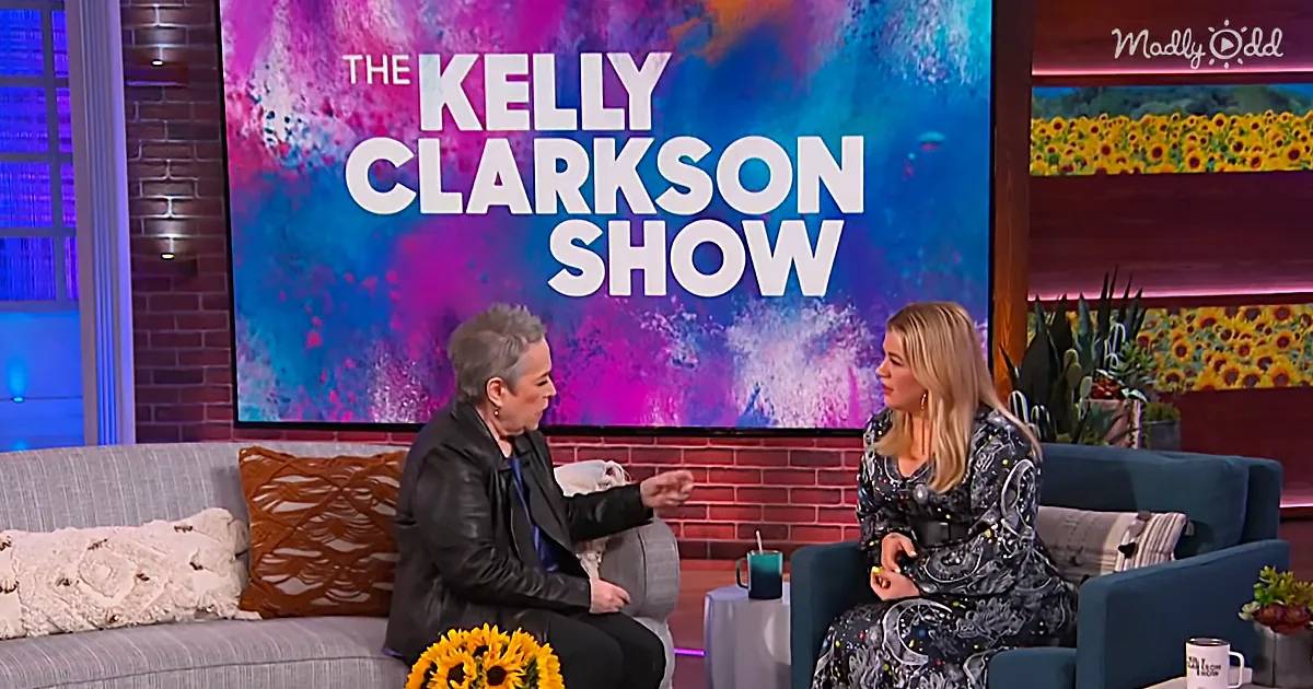 Kelly Clarkson and guest on "The Kelly Clarkson Show" set, colorful backdrop, floral decorations.