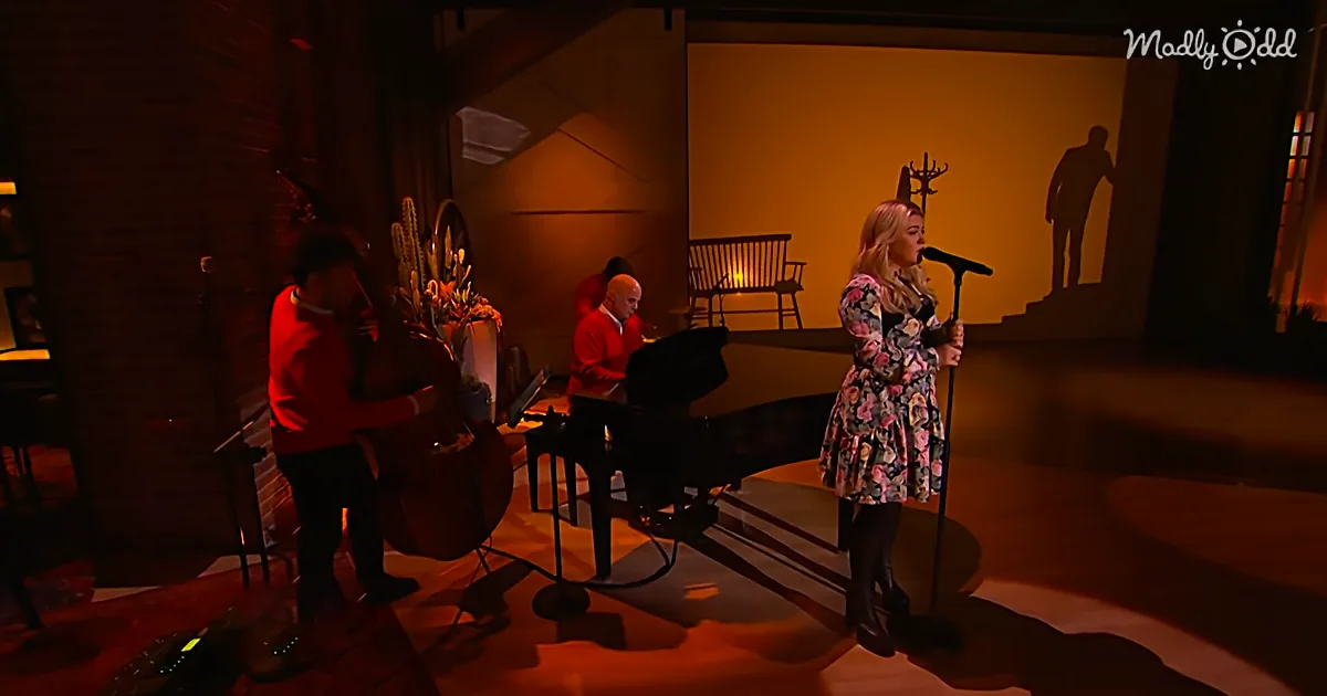 A woman in a floral dress sings into a microphone, accompanied by musicians playing cello and piano.