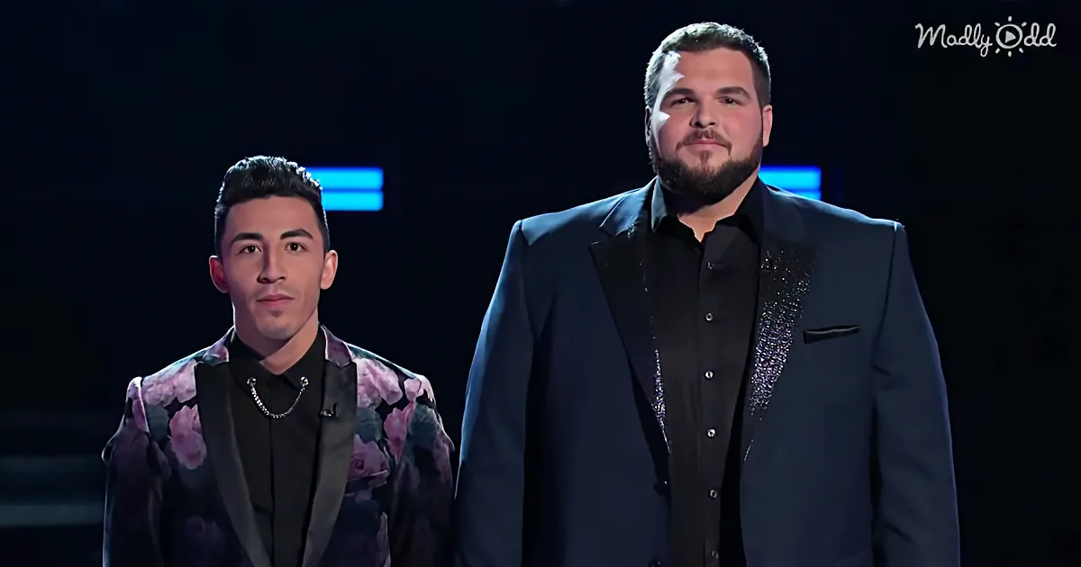 Two men in formal attire stand side by side, one in a floral suit, the other in a dark suit, against a dark background.