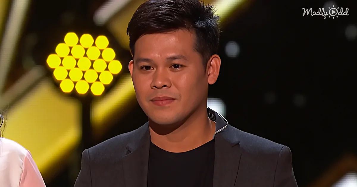 A man in a suit and black shirt sits in front of a yellow hexagonal light display.