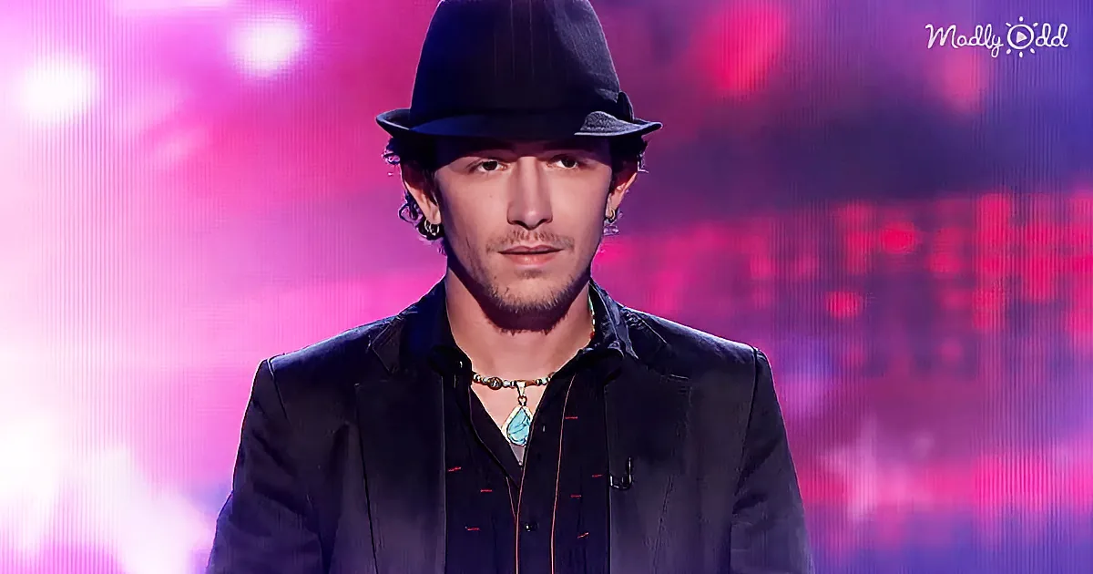 A man wearing a black hat and a dark suit stands against a vibrant, colorful background.