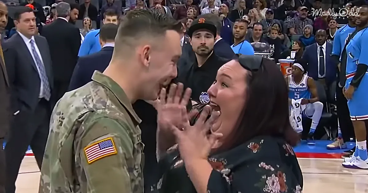 A soldier in camouflage uniform surprises a woman with a heartfelt embrace at a basketball game.