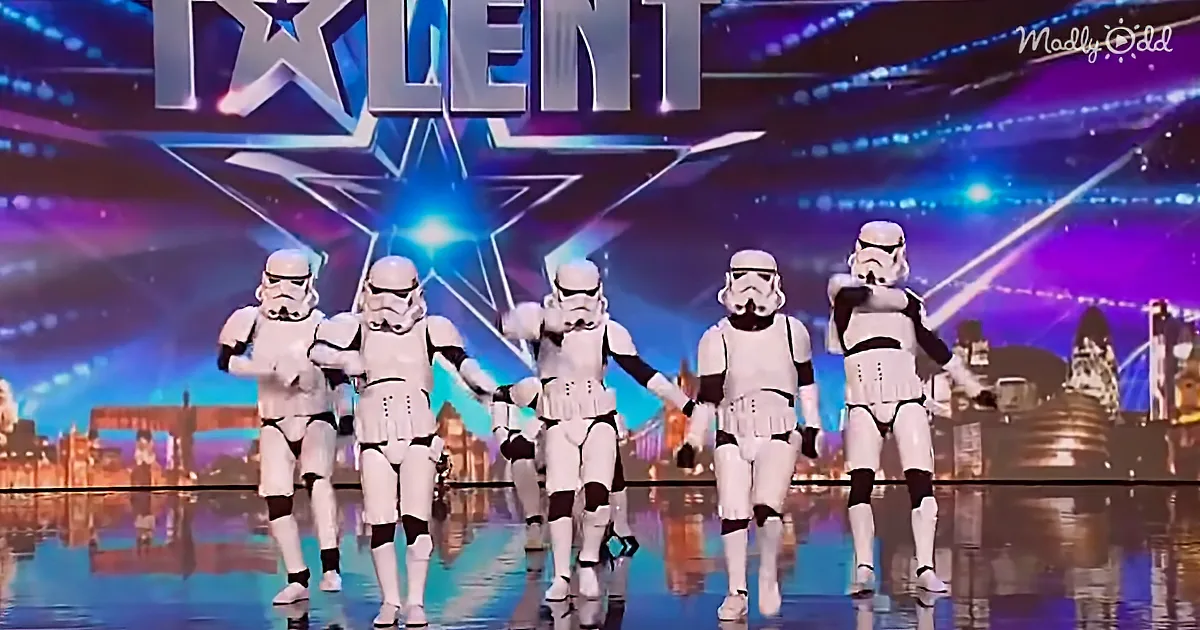 Five stormtroopers in white armor perform on a brightly lit stage with a "Talent" sign in the background.