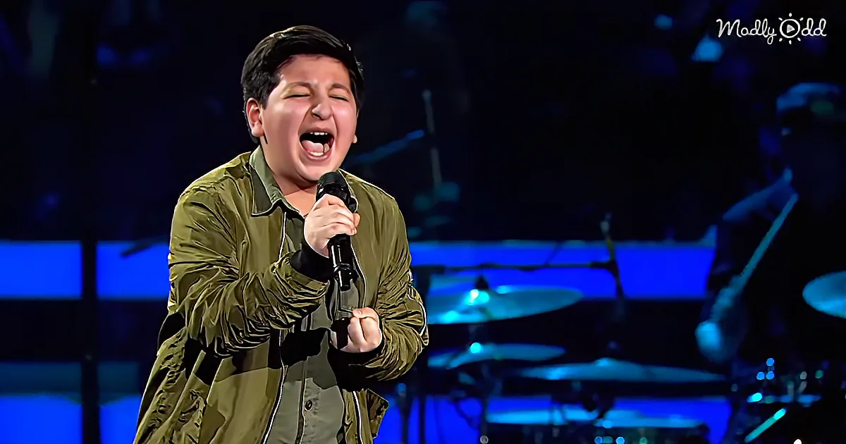 A young person in a green jacket sings passionately into a microphone on stage.