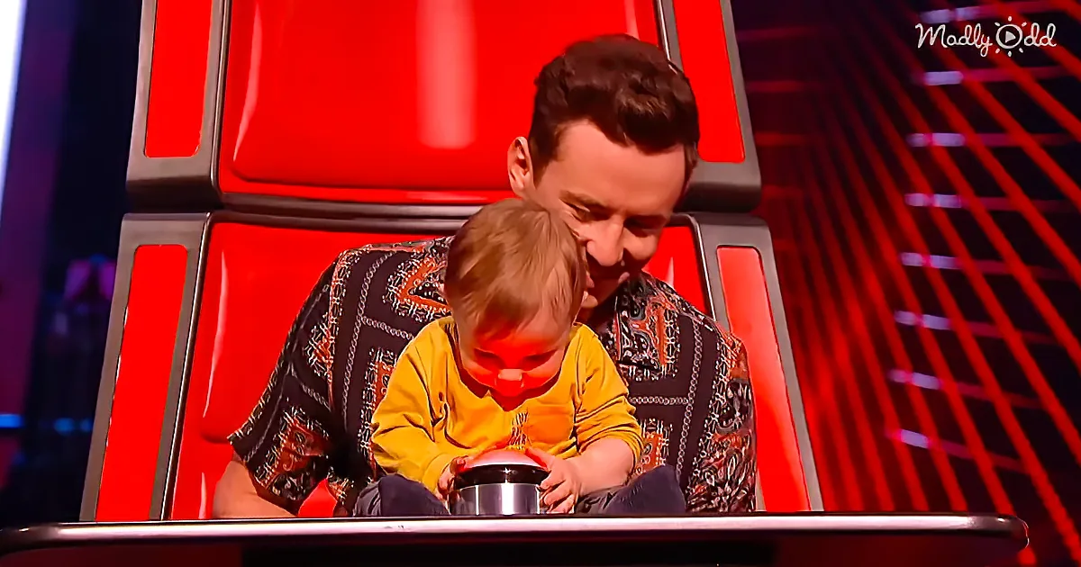 A man and a child sit together, the child holding a small object, both in a red-lit setting.