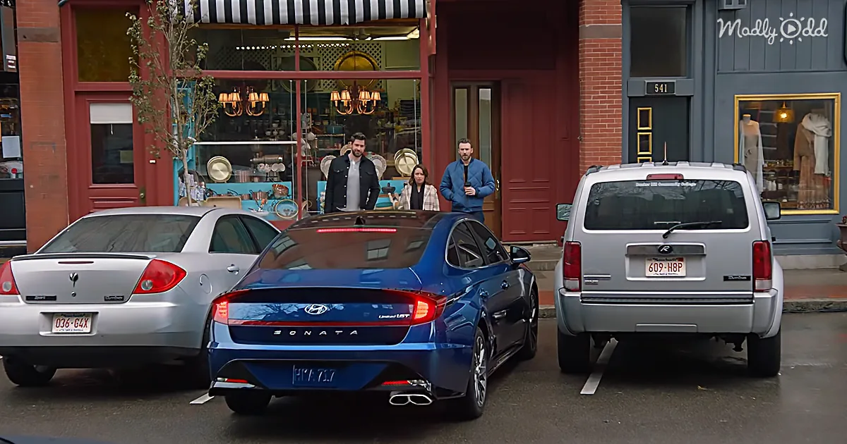 A blue Hyundai Sonata is parked between a silver sedan and a silver SUV in front of a store.