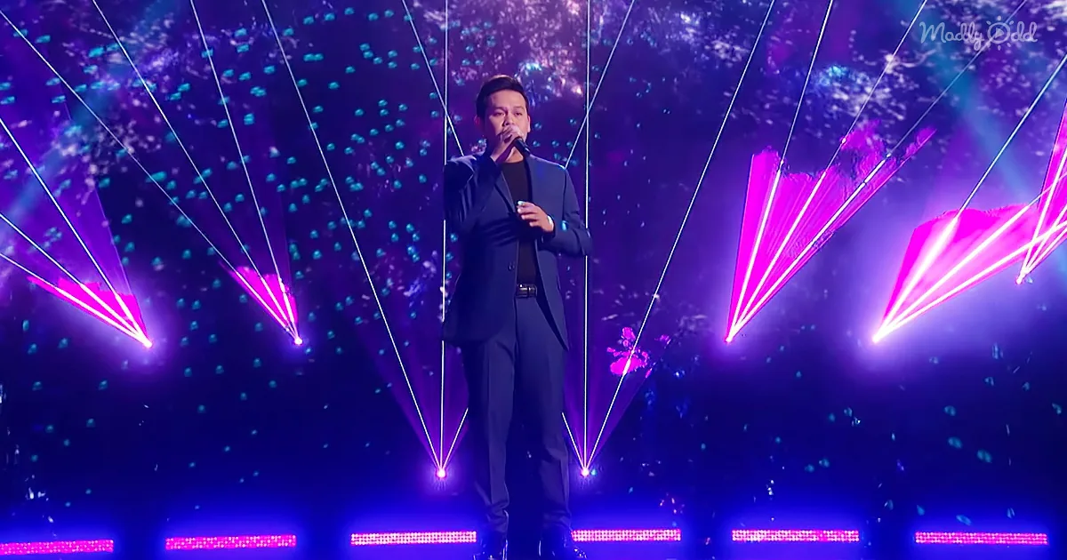 A man in a black suit sings on stage with vibrant purple and pink laser lights.
