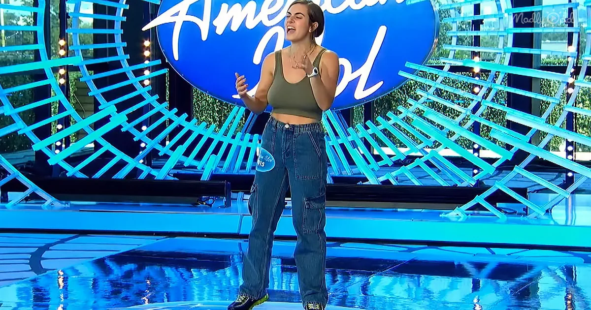 A person in a green crop top and jeans stands on a stage with a large "American Idol" sign behind them.