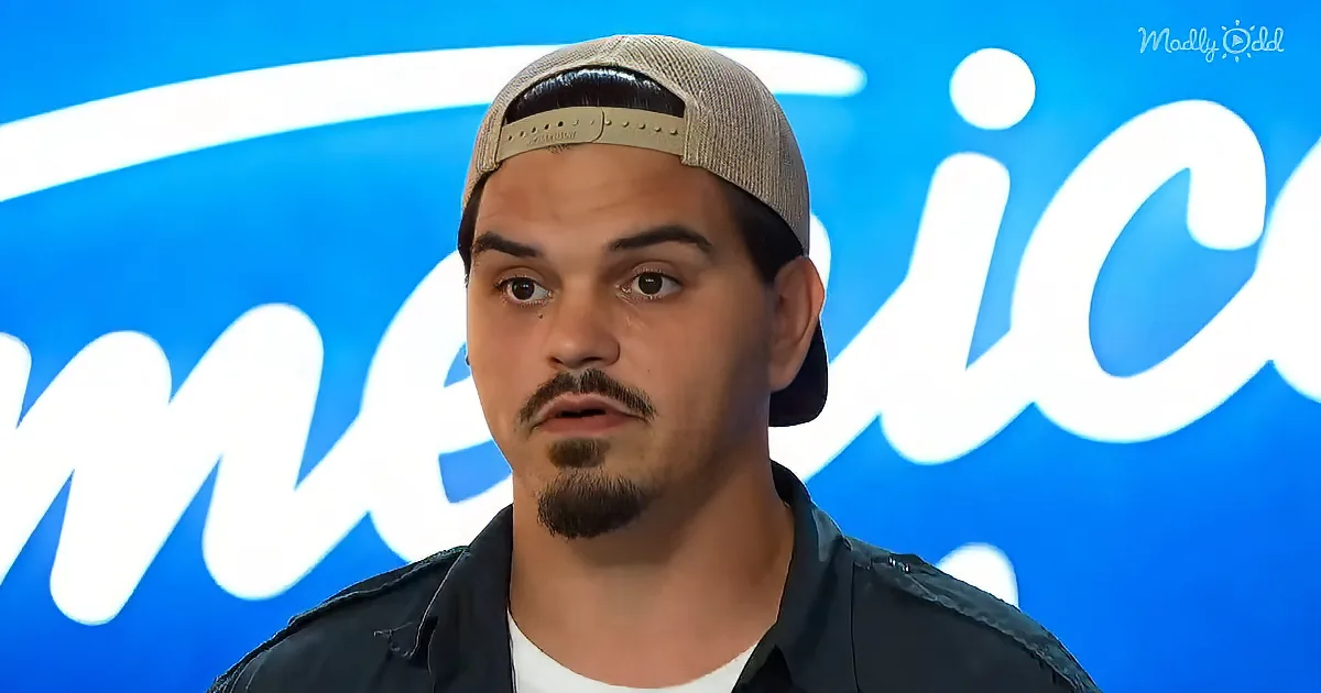 A man wearing a cap and a dark jacket stands in front of a blue background with "America" partially visible.