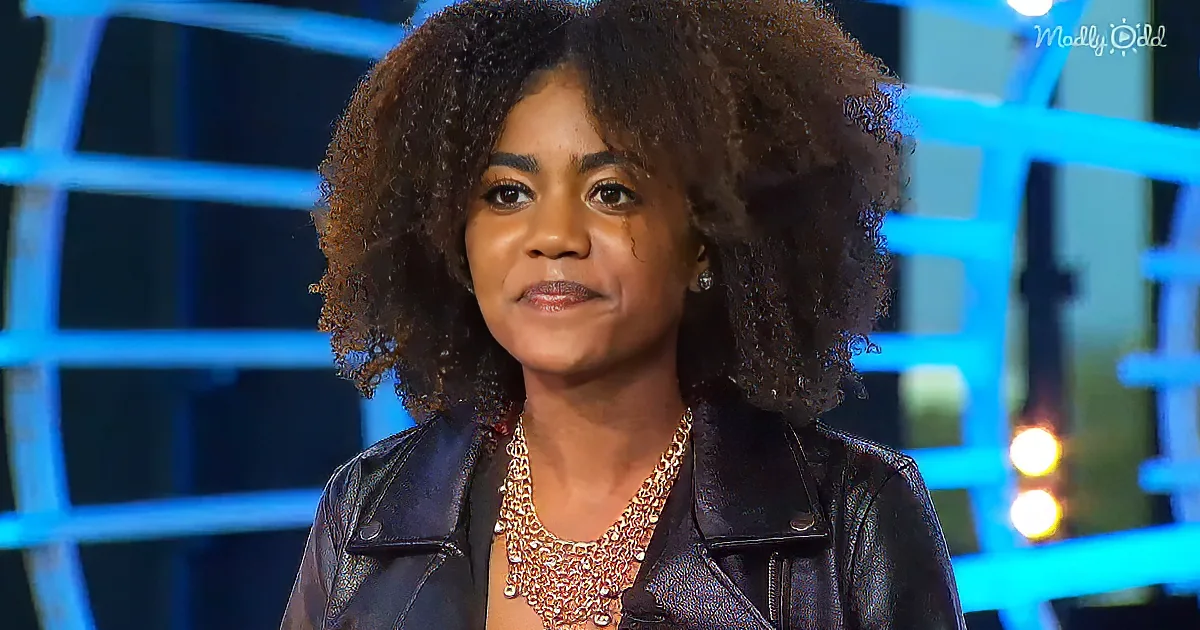 A woman with curly hair, wearing a black leather jacket and gold necklace, stands against a blue-lit background.