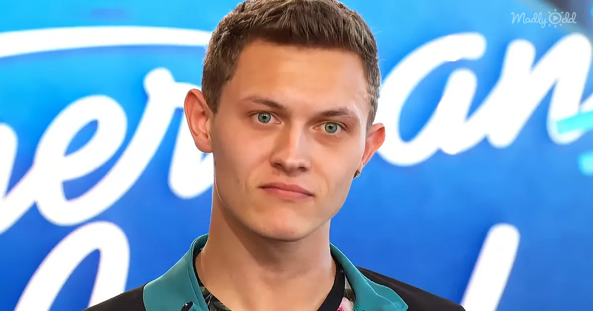 A person with short brown hair and blue eyes, wearing a black and teal shirt, stands in front of a blue background with...