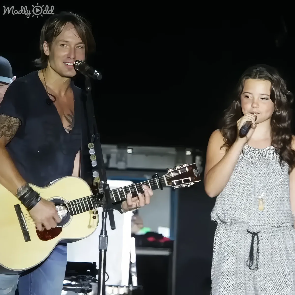 A man plays guitar while a woman sings into a microphone on stage.