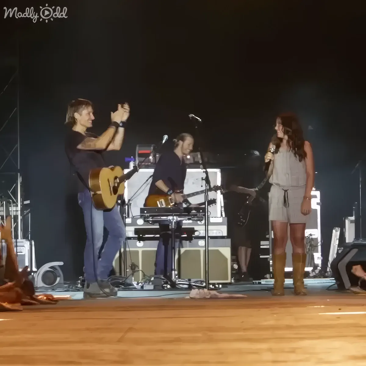 A man takes a photo of a woman holding a microphone on stage with musicians.