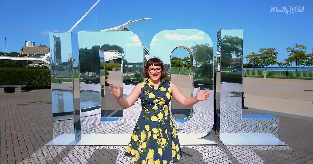 A woman in a lemon-print dress stands in front of large reflective letters spelling "MADLY."