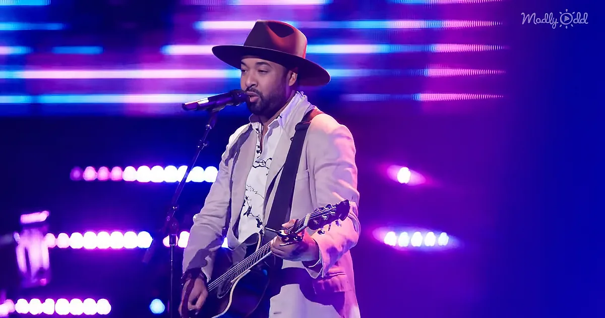 A man in a hat and suit plays guitar and sings on stage with vibrant purple and blue lights.