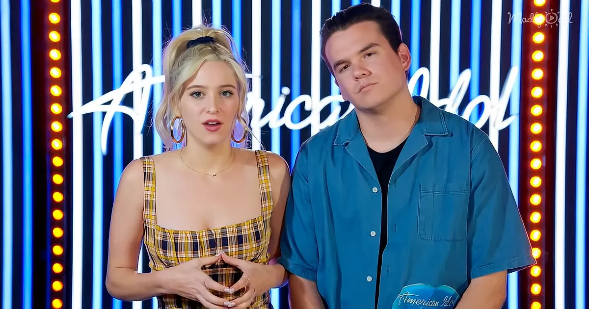 A woman in a plaid dress and a man in a blue shirt stand in front of a neon-lit "American Idol" backdrop.