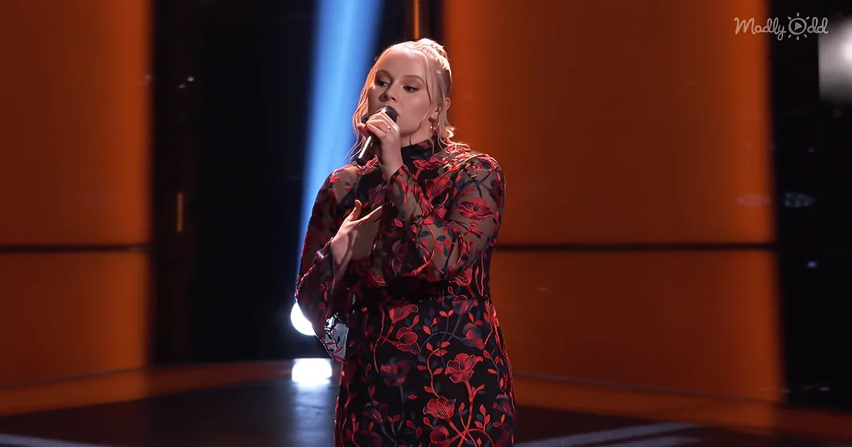 A woman in a red floral dress sings into a microphone on a stage with orange lighting.