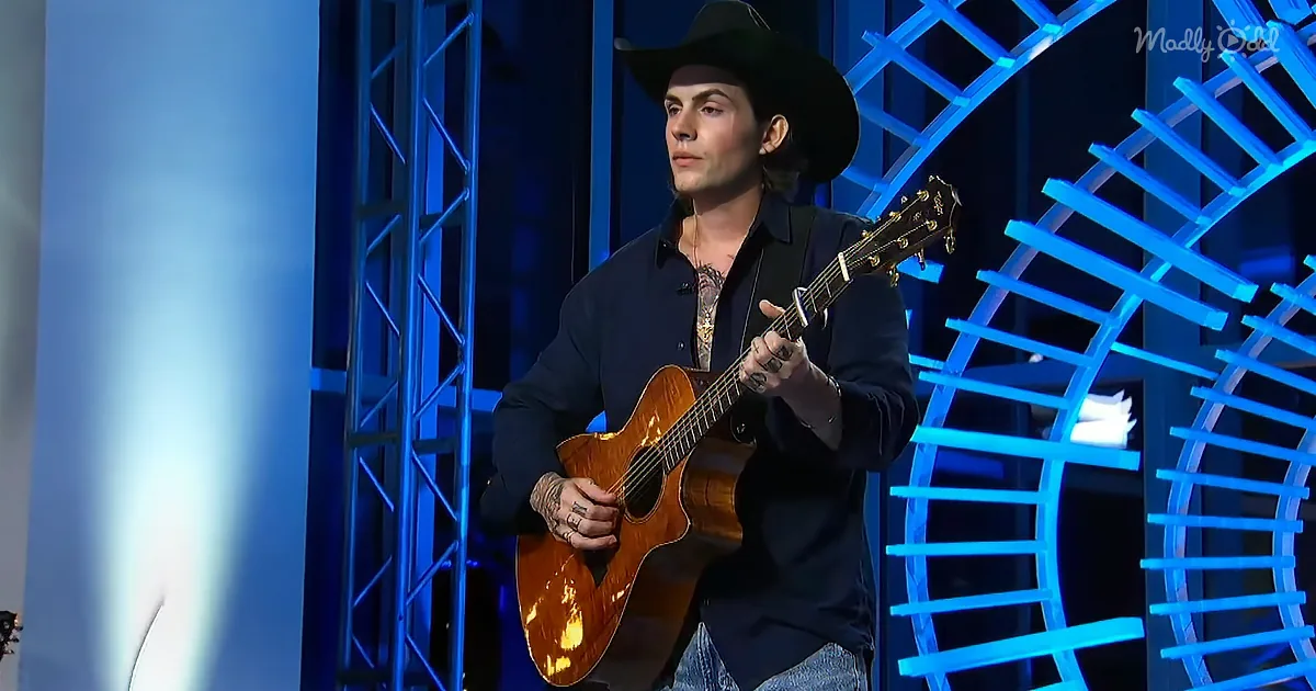 A man in a cowboy hat plays an acoustic guitar on stage with blue lighting.