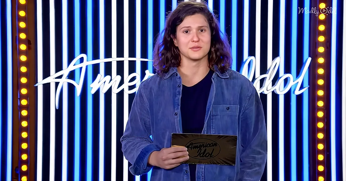 A person stands in front of an "American Idol" backdrop holding a card.