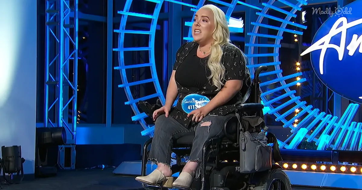 A woman with long blonde hair sits in a wheelchair on a stage with blue lighting and an "American Idol" sign.