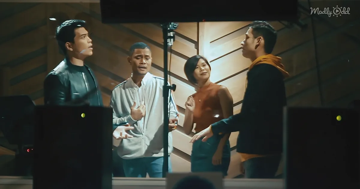 Four individuals in a recording studio, one gesturing, others listening, with microphones and equipment visible.