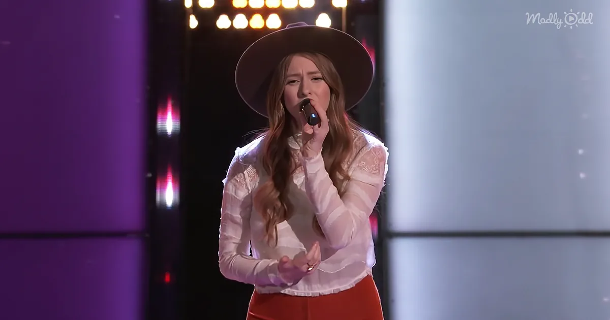 A woman in a white lace top and red pants sings into a microphone on stage.