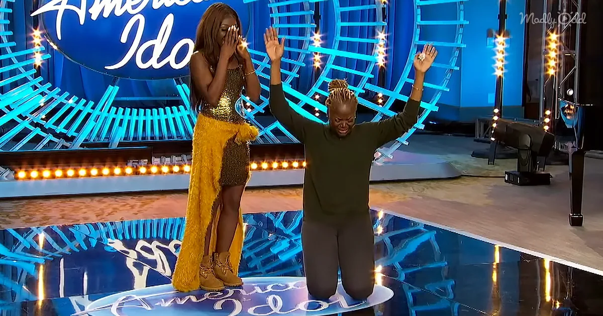 Two women on stage, one kneeling in victory, the other covering face, both on "American Idol" set.