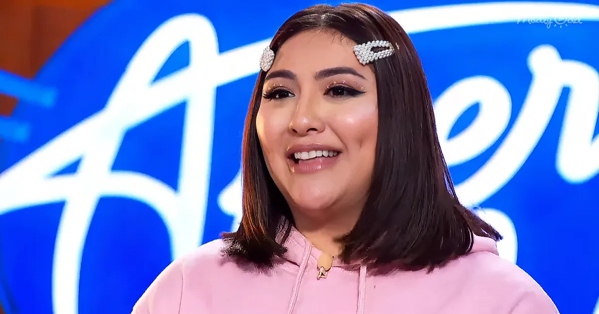 A smiling woman with dark hair, wearing a pink hoodie and pearl hair clips, stands in front of a blue background with...