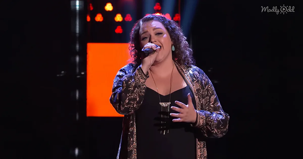 A woman sings passionately on stage, wearing a patterned jacket and black dress, with a glowing orange background.
