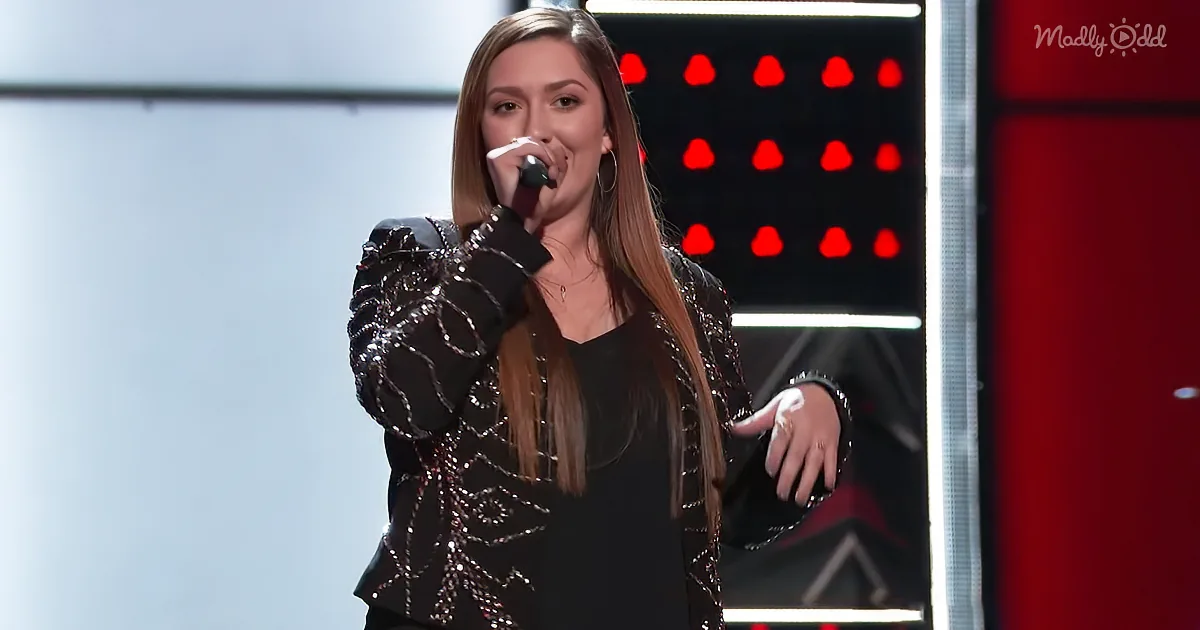 A woman sings into a microphone, wearing a black sequined jacket, on a stage with red lights in the background.