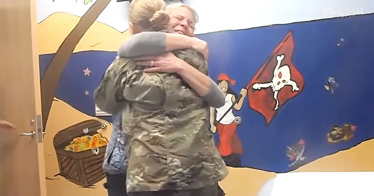 Two women in a heartfelt embrace, one in camouflage, against a colorful pirate-themed mural.