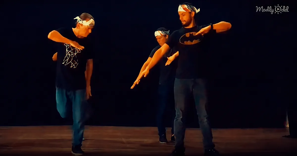 Three dancers in casual attire perform synchronized moves on a dimly lit stage.