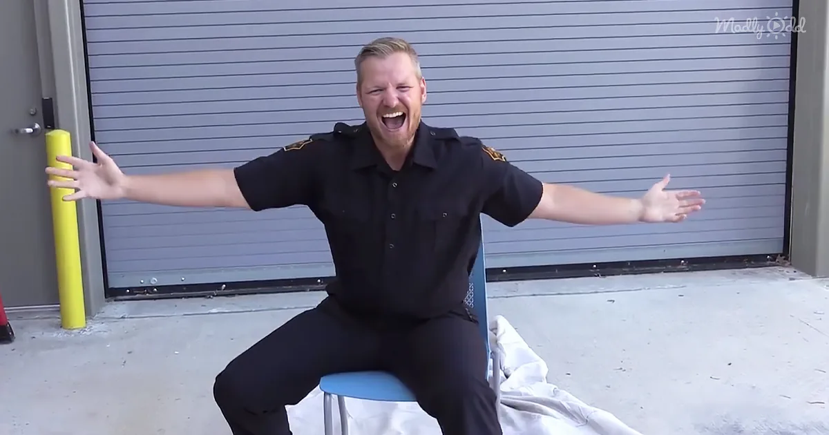 A man in a black uniform sits on a chair, arms outstretched, in front of a garage door.