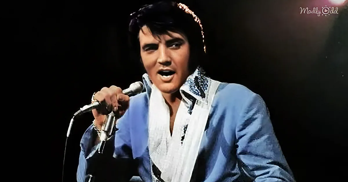 Elvis Presley in a blue suit sings into a microphone on stage.