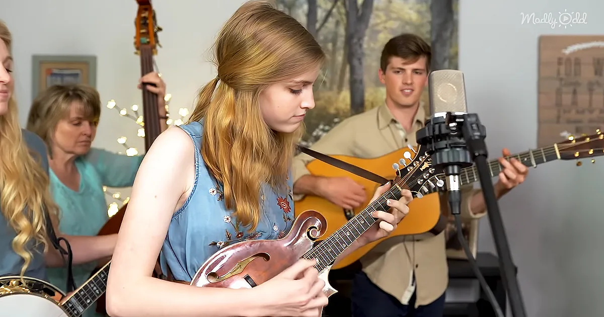 A young woman plays a mandolin in front of a microphone, surrounded by other musicians.