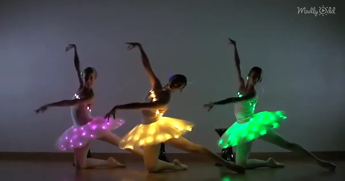 Three dancers in glowing tutus perform a split, illuminated by colorful lights.