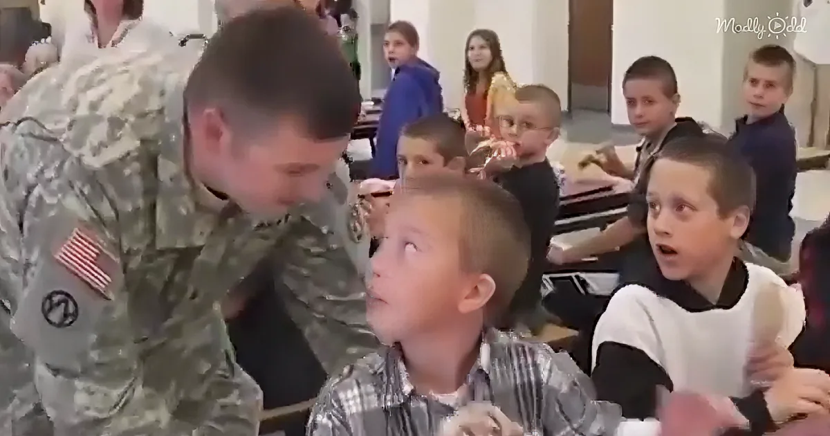 A soldier in camouflage greets a young boy in a classroom, surrounded by other children.