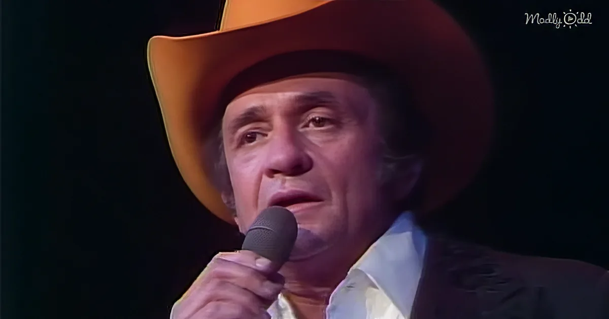 A man in a cowboy hat sings into a microphone, wearing a patterned shirt.