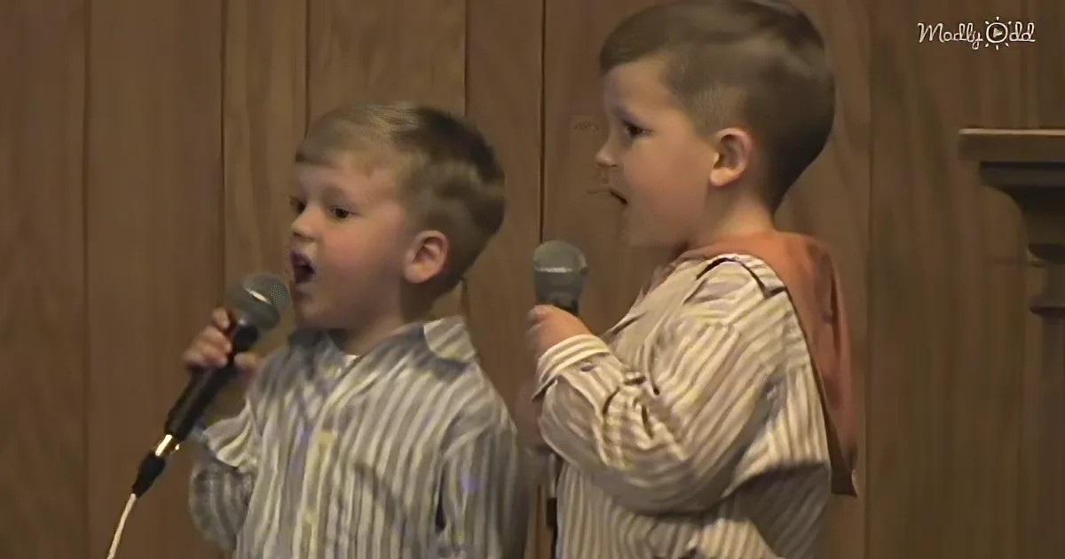 Two young boys in striped shirts sing into microphones, one with a surprised expression.