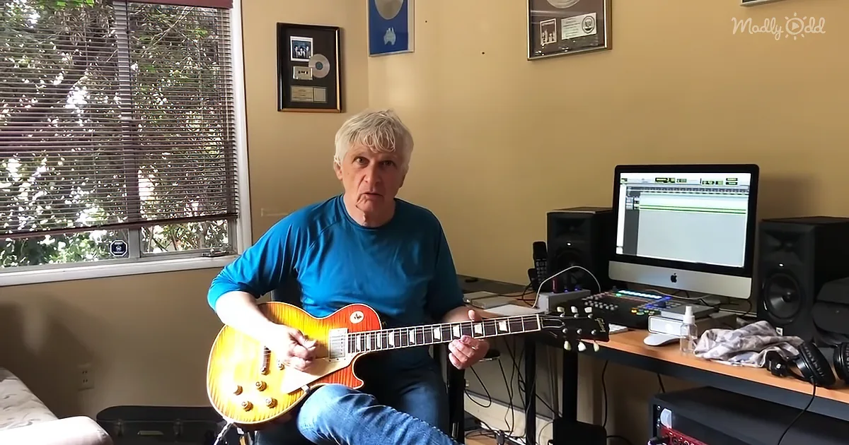 Man in blue shirt plays yellow electric guitar in room with computer and speakers.
