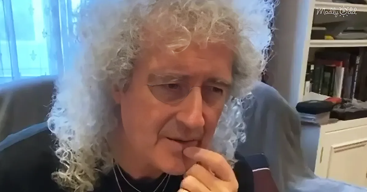 A person with curly white hair and a black shirt is holding a microphone, seemingly speaking or singing.
