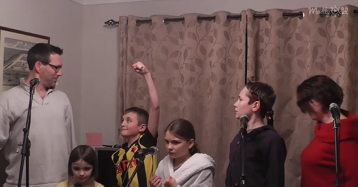 A man stands with children, one raising their fist, in a room with curtains and microphones.