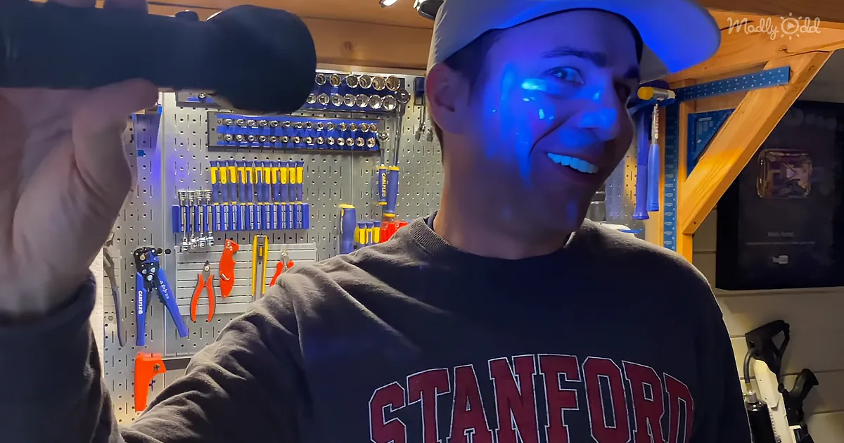 A man in a Stanford sweatshirt smiles in a well-lit workshop with tools and a pegboard.