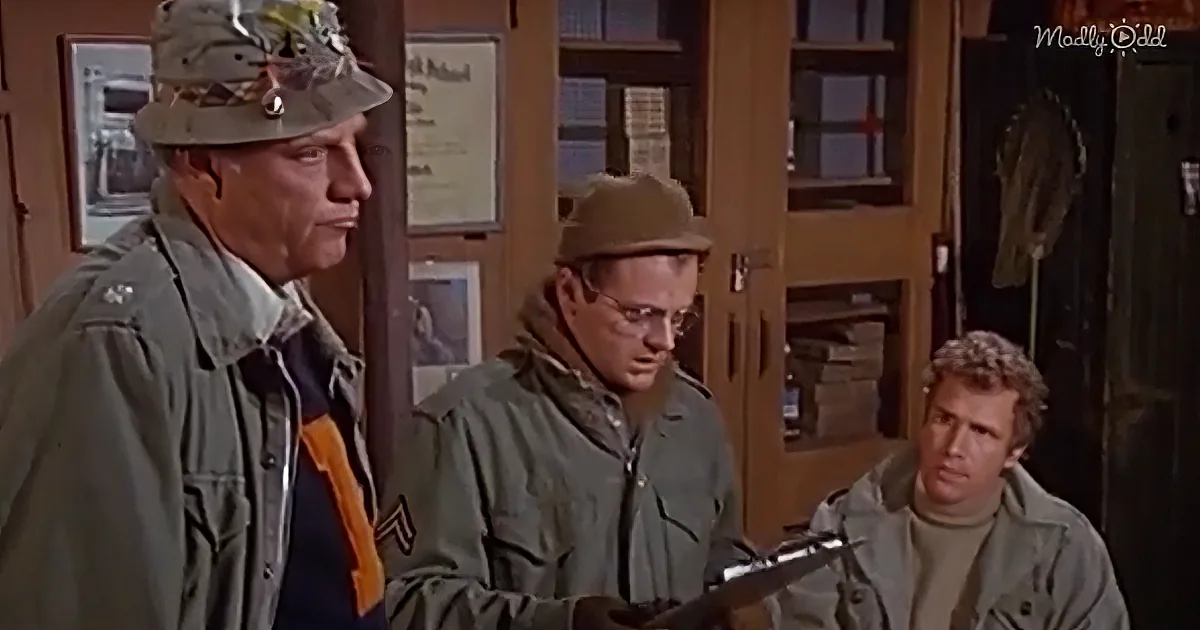 A man in a military uniform and hat stands beside another in a green jacket and glasses, holding a clipboard, while a...