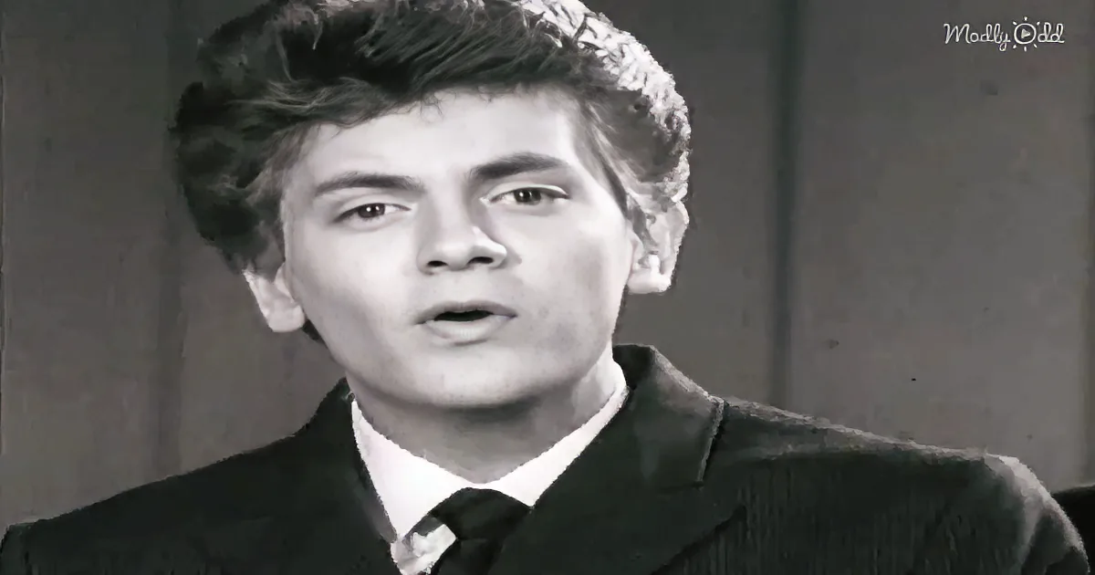A man in a suit and tie, with curly hair, appears to be speaking or reacting to something.