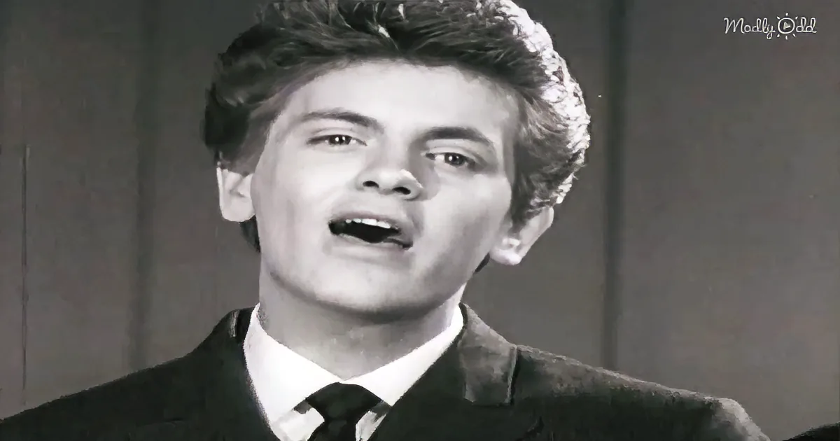 A man in a suit and tie is singing, with his mouth open and a focused expression.