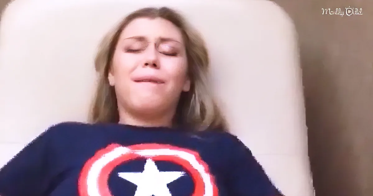 A person wearing a Captain America shirt lies on a white surface with eyes closed.
