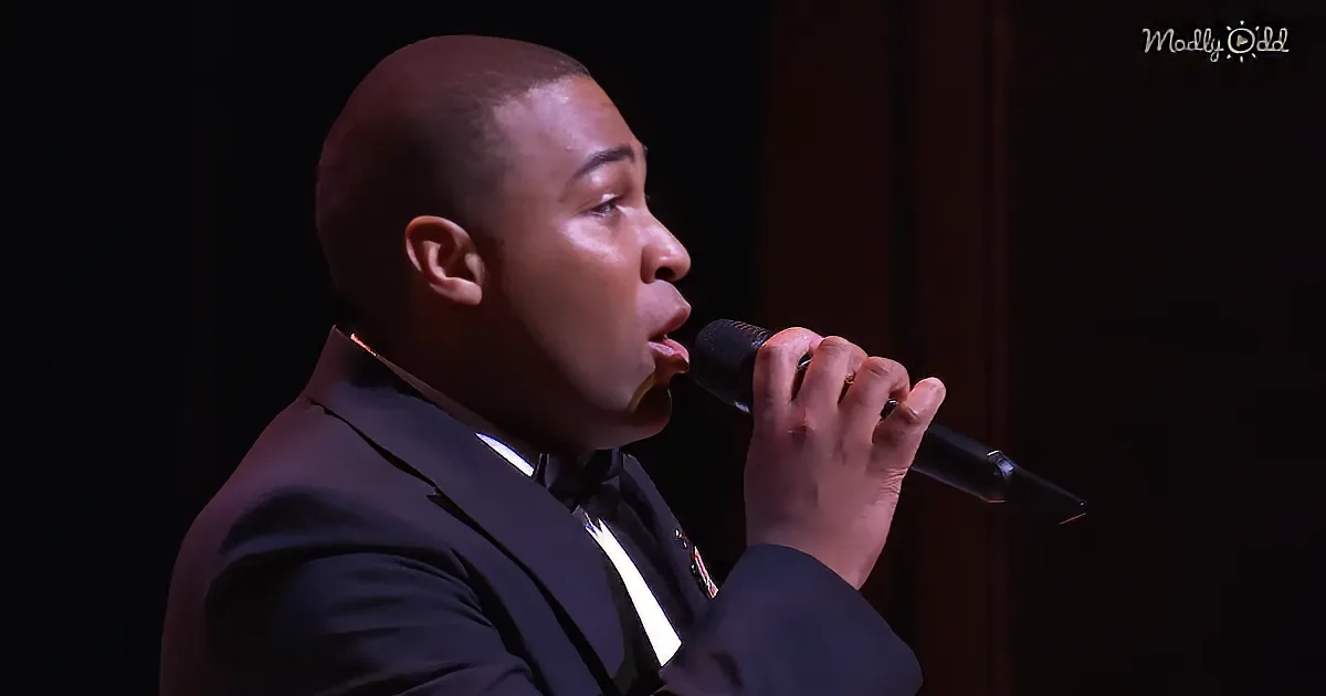 A man in a suit sings into a microphone on stage.